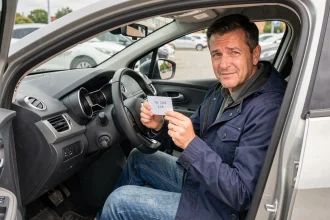 Homme assis dans une Renault Clio 4 tenant un code d'authentification inscrit sur une carte, prêt à démarrer le véhicule