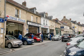 Vue d'ensemble d'une rue de garages automobiles indépendants dans le Loiret, avec des mécaniciens en blouse bleue travaillant sur des véhicules