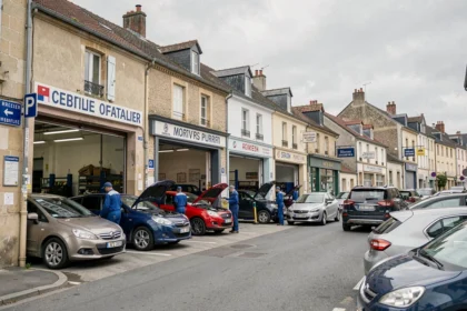 Vue d'ensemble d'une rue de garages automobiles indépendants dans le Loiret, avec des mécaniciens en blouse bleue travaillant sur des véhicules